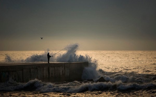 Людина на пірсі ловить рибу в Середземному морі в Барселоні, Іспанія. (© AP)