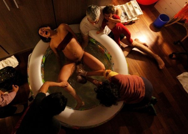 Акушерки допомагають Мануелі Мітре народити другу дитину Гаель у басейні з водою, в той час як її чоловік Андре (2-й праворуч) і донька Еліс дивляться, Сан-Паулу, 6 листопада 2013. NACHO DOCE, Бразилія