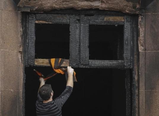 місцевий житель прив’язує  чорно-помаранчеву стрічку -  символ, який  пов'язаних з проросійськими акціями в Україні, до згорілого Будинку профспілок