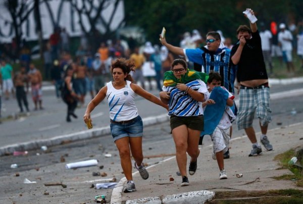 Сім'я з квитками на матч біжить в укриття, опинившись між поліцією і протестувальниками перед стадіоном незадовго до матчу між Нігерією та Уругваєм в Сальвадорі, 20 червня 2013. KAI PFAFFENBACH, Бразилія